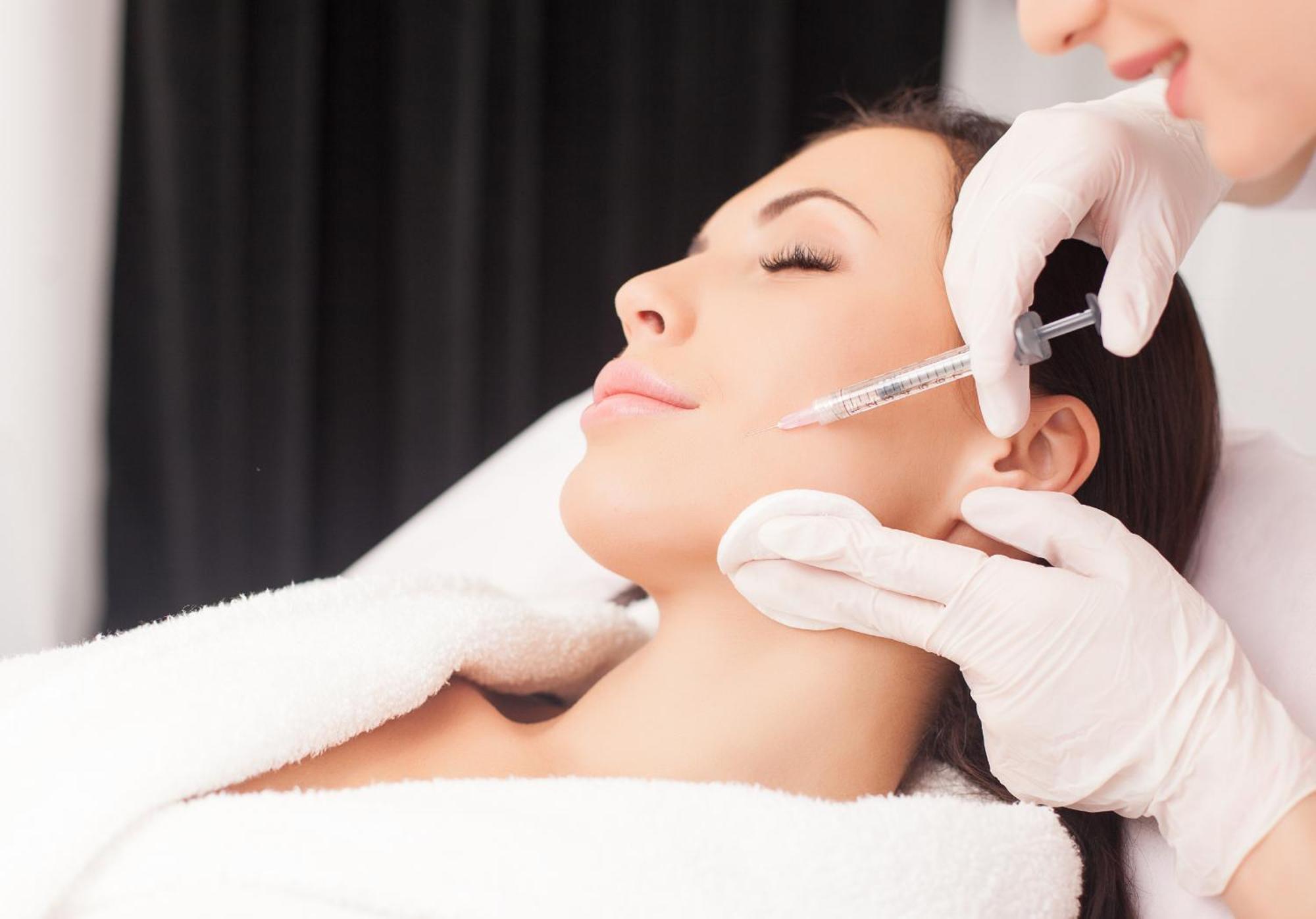 Grandhotel Pupp Karlsbad Buitenkant foto The photo depicts a woman receiving a cosmetic treatment in a spa or clinical setting. She is reclining with her eyes closed, appearing relaxed. A professional, wearing gloves, is administering an injection to her face, likely as part of a procedure 