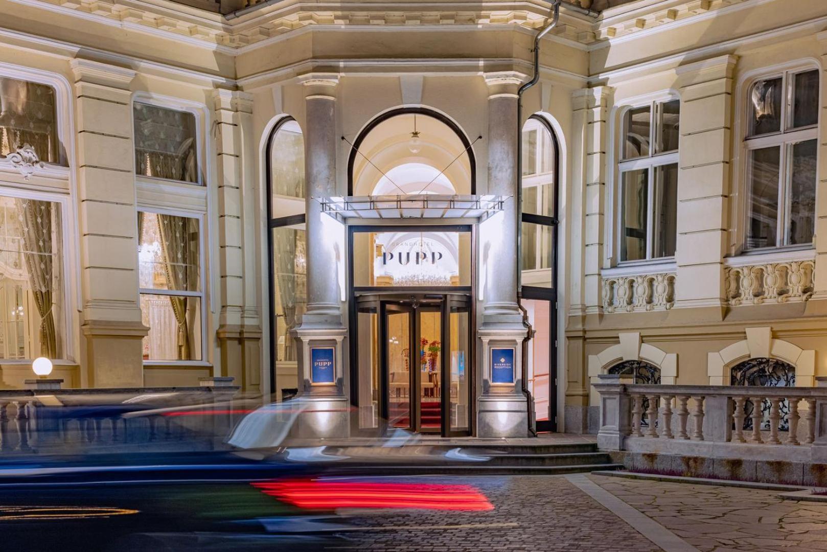 Grandhotel Pupp Karlsbad Buitenkant foto The photo depicts the entrance of a building, likely a theater or cultural venue, at night. The facade features a classic architectural style with decorative elements. The entrance has a pair of double doors framed by large windows, and there is a pr